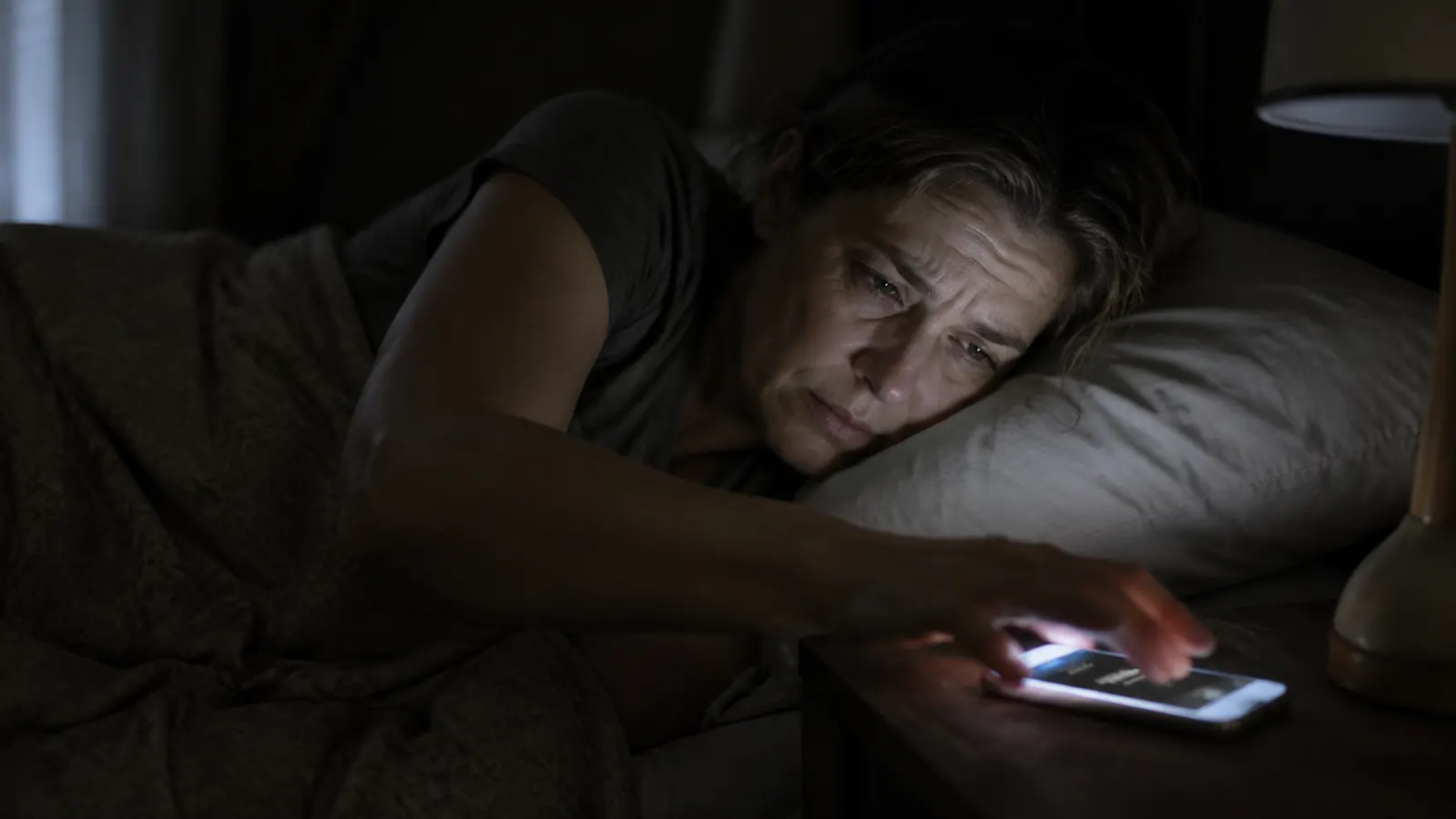 Soft warm amber light filling a dark bedroom at dawn, with a sunrise alarm clock glowing on a nightstand beside a sleeping adult