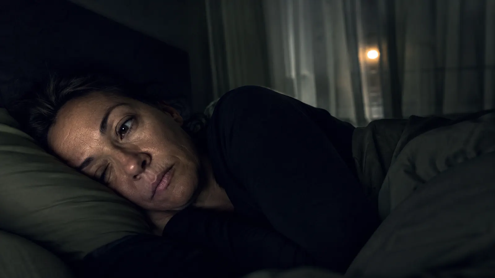 Person sleeping peacefully in a dark bedroom with a sound machine on the nightstand