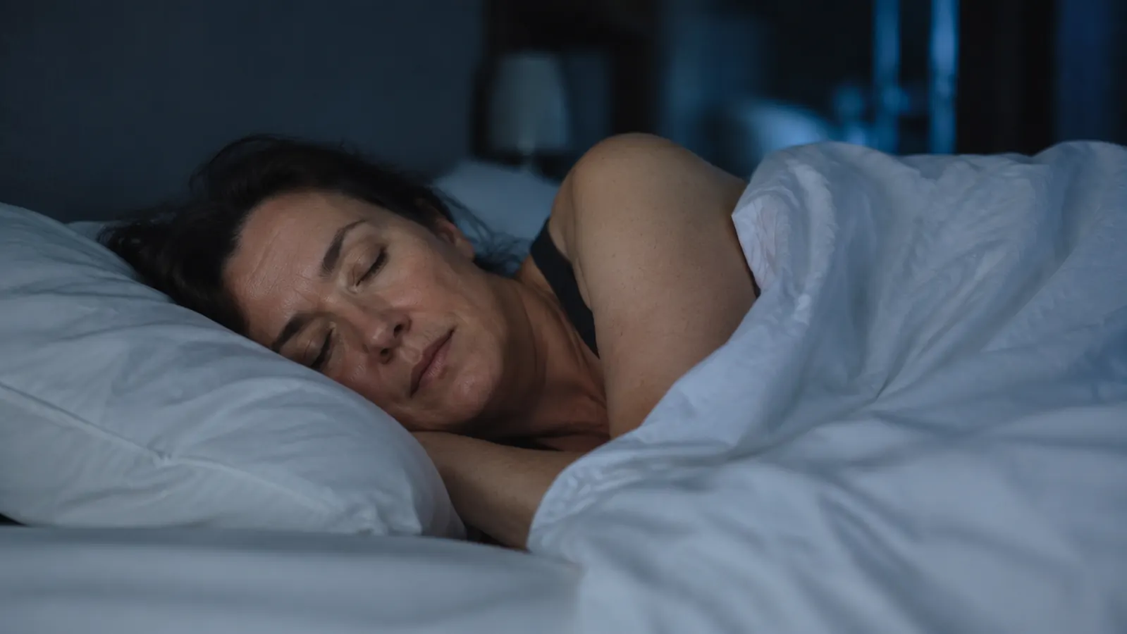 Woman sleeping peacefully on her side under a thin sheet with a bright bedside clock showing 3am, no sweat, relaxed expression